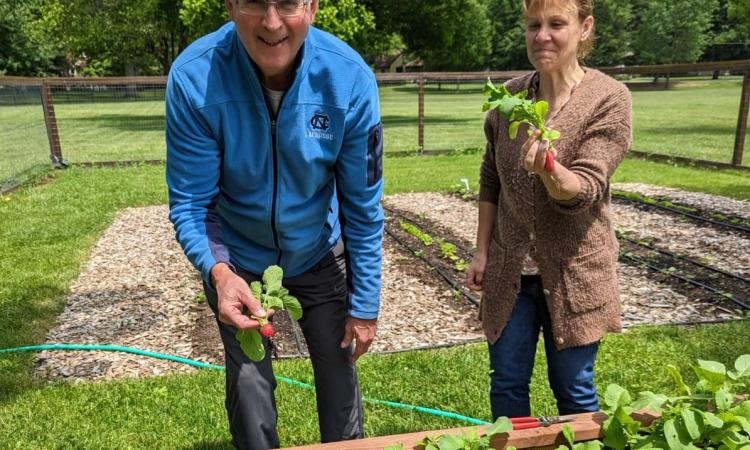 Two gardeners proudly holding freshly harvested radishes in front of the community garden at First Presbyterian Church