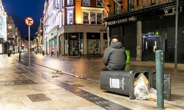 A lone man sits in an empty city street during a severe winter storm. His isolation mirrors the human cost of inaction, as extreme weather and inequality grow side by side.